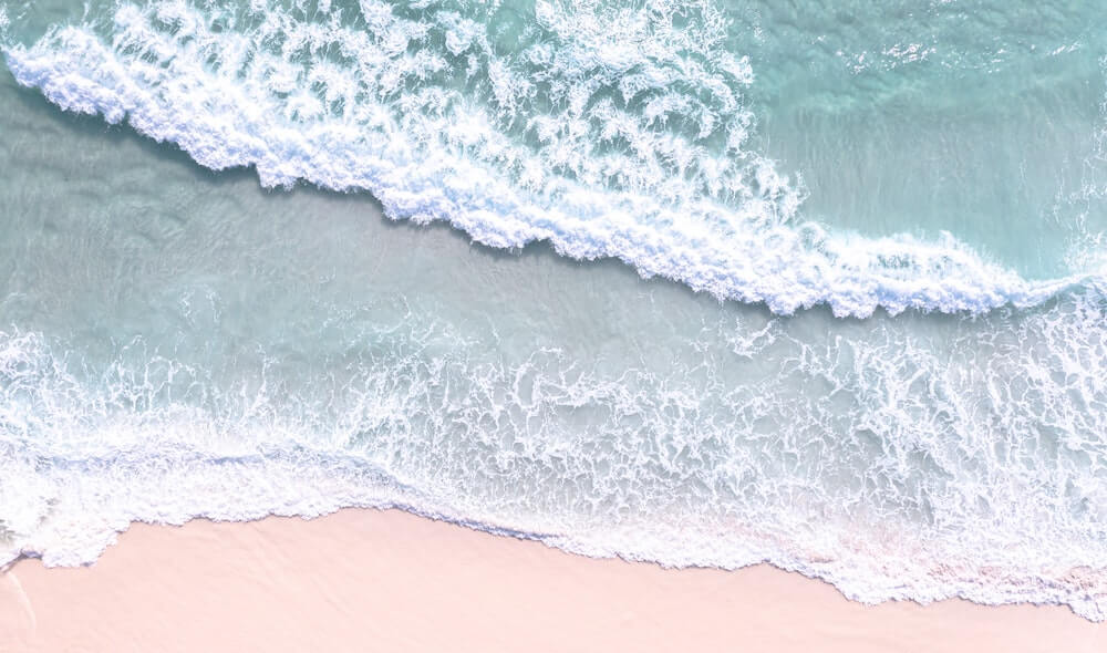 Foto de drone das ondas da praia, uma agua bem azul e areia clara