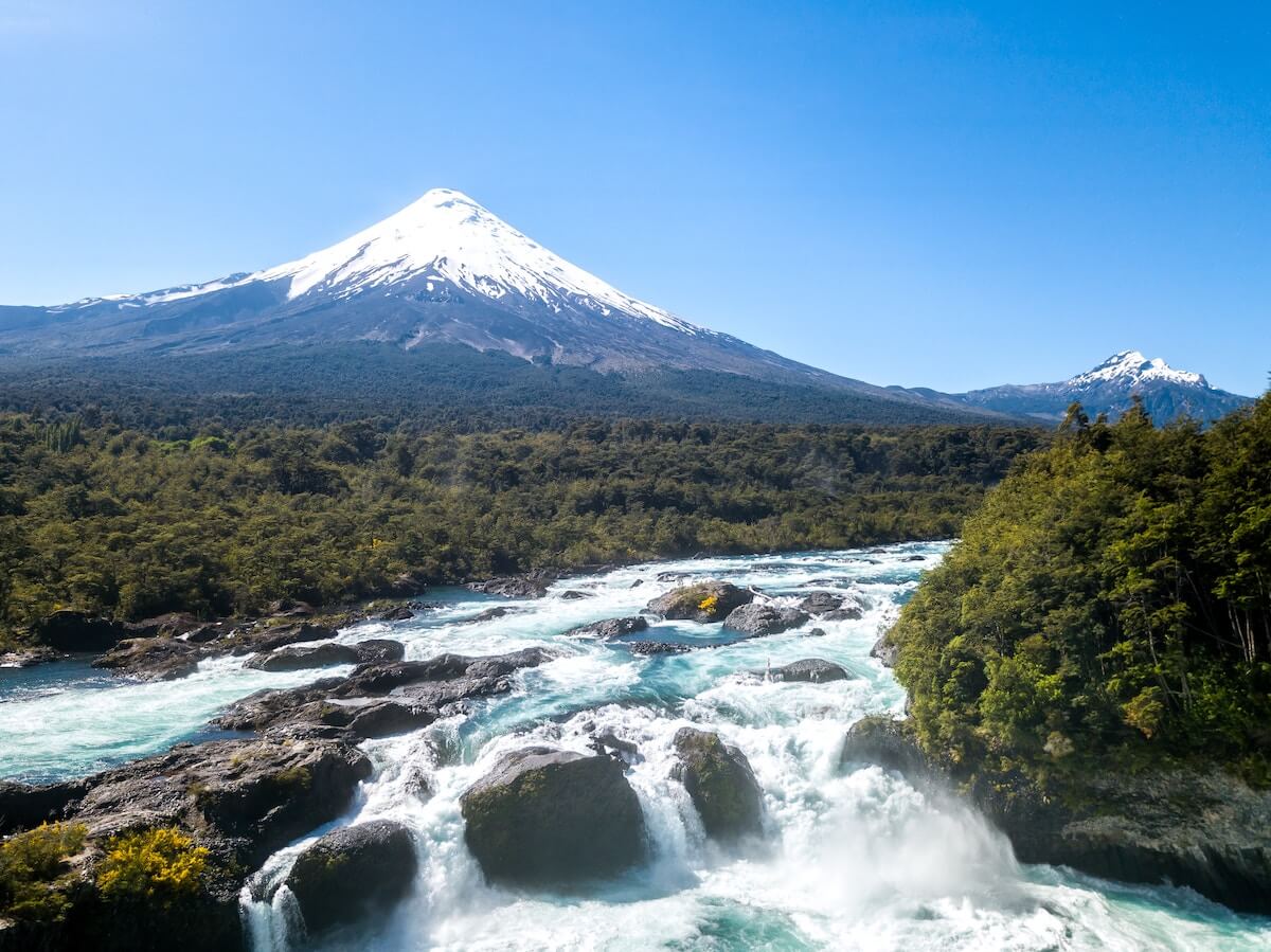 Um rio muito bonito com  a imagem de um vulcão enorme atrás.
