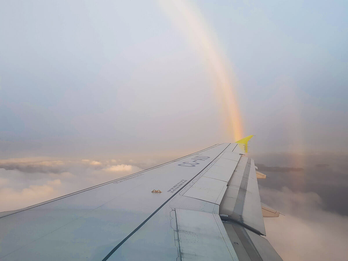 Foto da asa do avião com um arco íris