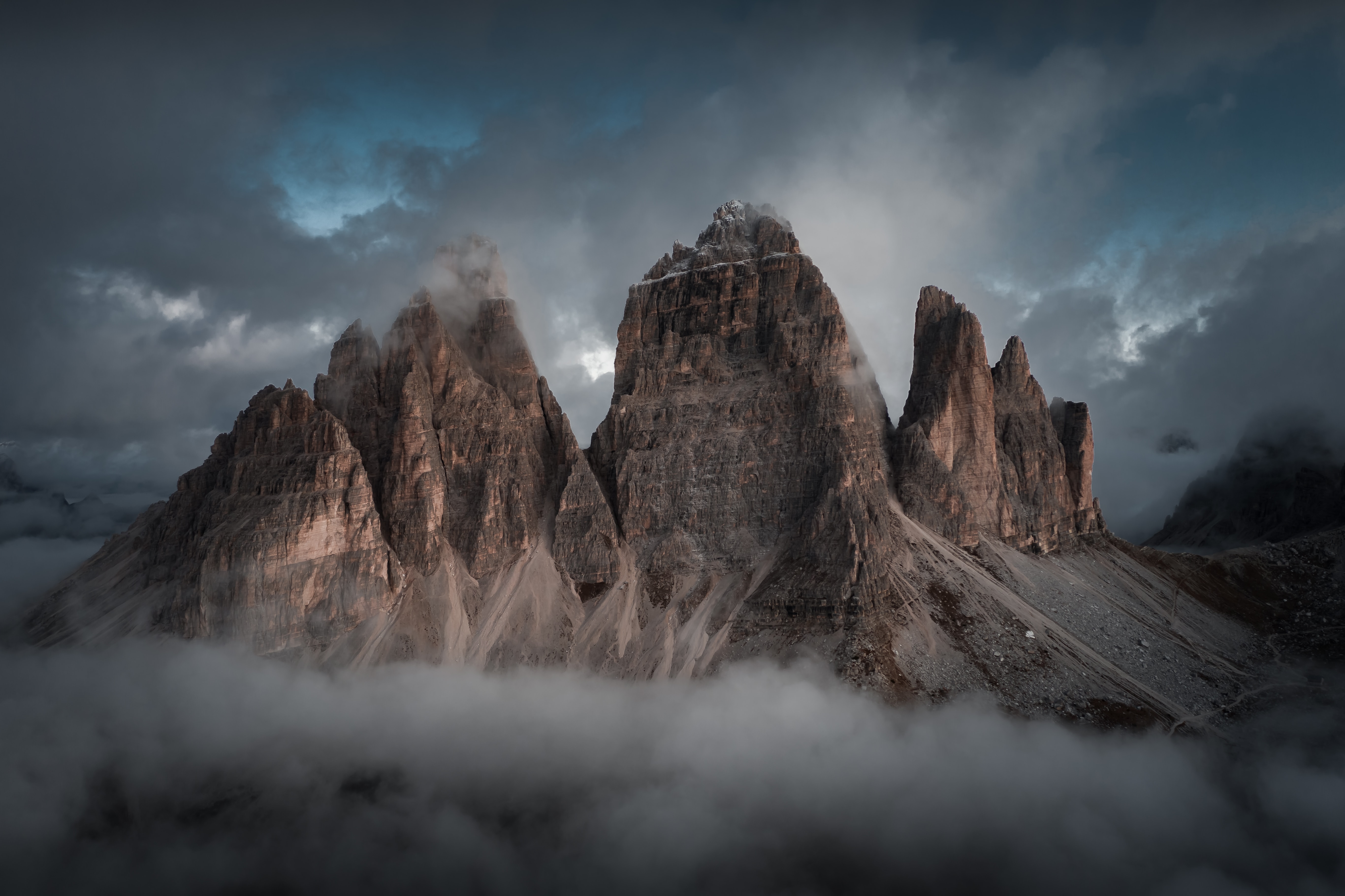 Foto do Tre Cime di Lavaredo, que é uma montanha com 3 picos, estava amanhecendo, porém ainda escuro e com névoa na parte inferior.